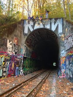 people are standing on the top of a train tunnel with graffiti all over it and trees in the background