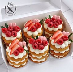 a box filled with lots of cupcakes covered in frosting and topped with raspberries