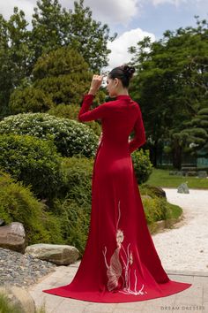 a woman in a long red dress taking a photo with her cell phone while standing outside