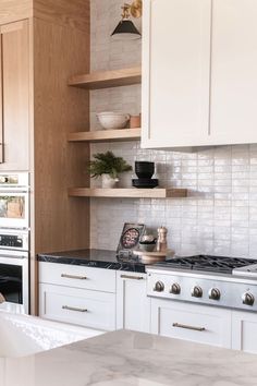 a kitchen with white cabinets and marble counter tops, along with open shelving above the stove