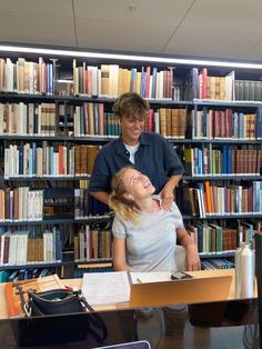 two people in a library with bookshelves full of books and one woman is laughing