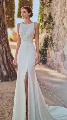 a woman standing in front of a tree wearing a white dress with high slits