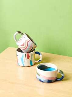 two cups sitting on top of a wooden table next to each other, one with a teapot in it