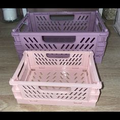 two plastic crates sitting next to each other on a wooden floor, one is purple and the other is pink