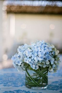 a glass vase filled with blue flowers on top of a table covered in blue and white cloth