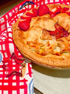 a pie with strawberries and other toppings on a red and white checkered table cloth