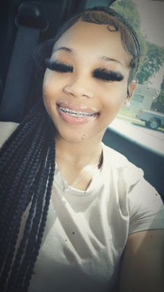 a woman with long braids smiling in the back seat of a car while wearing a white t - shirt