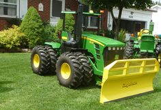 two green tractors parked in the grass with yellow plow attachments on each side