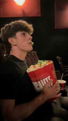 a young man sitting in a movie theater holding a box of popcorn