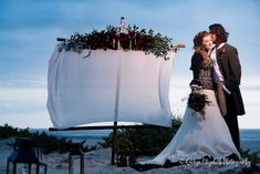 a bride and groom kissing in front of an outdoor wedding ceremony set up on the beach