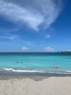 people are swimming in the ocean on a sunny day with blue skies and white clouds