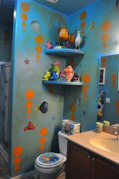 a bathroom decorated in blue and orange with fish on the wall, shelves above the toilet