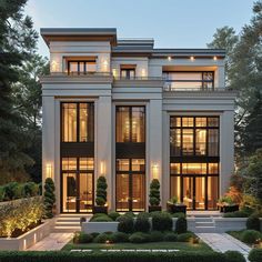 a large white house with lots of windows and plants in the front yard at night