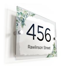 a white sign with black numbers and green leaves on it's sides is mounted to the wall