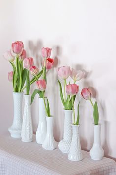 four white vases filled with pink tulips on a checkered table cloth