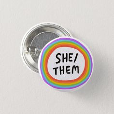 a button that says she / them on it with a rainbow in the middle and black letters