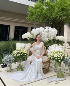 a woman is sitting on a chair in front of some white flowers and greenery