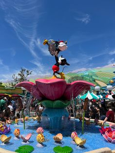 the mickey mouse water fountain is decorated with colorful flowers and fish in front of a blue sky