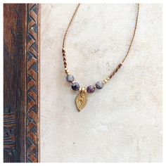 a necklace with beads and a gold leaf charm hanging from it's side on a wooden surface