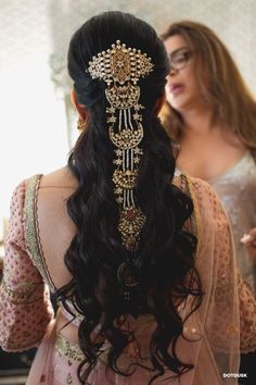 the back of a woman's head with long hair and jewelry on it, in front of a mirror