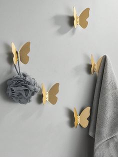 three butterfly hooks hang on the wall next to a gray towel and folded grey towels