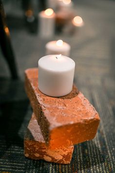 two white candles sitting on top of a piece of red brick next to each other