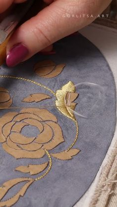 a woman is working on an embroidered design with gold thread and scissors in her hand