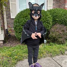 a young boy wearing a cat mask and purple shoes standing in front of a house