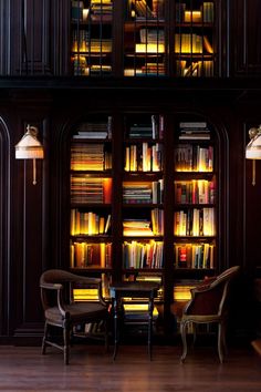 a room filled with lots of books next to two chairs and a table in front of a book case