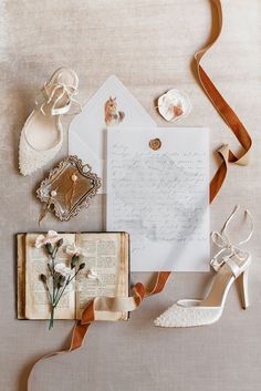 an assortment of wedding accessories including shoes, ring and letter on top of a table