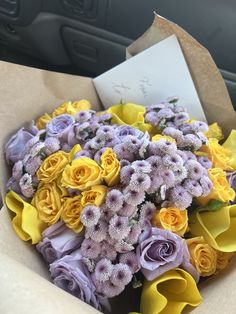 a bouquet of yellow and purple flowers in a brown paper bag on the back seat of a car