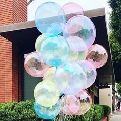 a bunch of balloons that are in front of a building and some bushes on the sidewalk