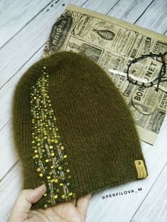 someone is holding up a green beanie with beaded details on it and next to the hat