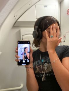 a woman holding up her cell phone to take a selfie in the mirror on an airplane