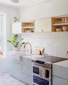 a kitchen with a stove, sink and counter tops in white tiled space between two open shelving units