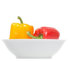 two peppers in a white bowl on a white background with one red and one yellow pepper