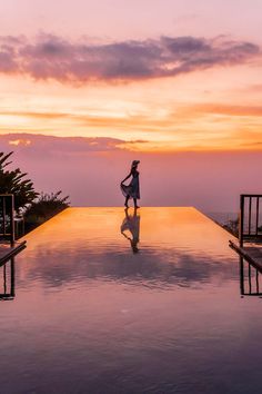 a woman standing on the edge of a pool at sunset