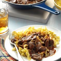 a white plate topped with pasta and mushrooms next to a glass of beer on a table