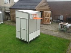 an outhouse in the middle of a yard with grass and other houses behind it