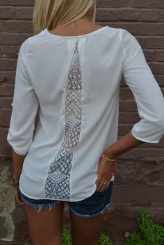 a woman standing in front of a brick wall wearing a white shirt with an intricate tie on it