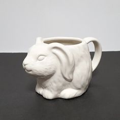 a white ceramic animal mug sitting on top of a black table next to a wall