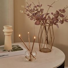 two vases filled with flowers on top of a table next to a book and candle