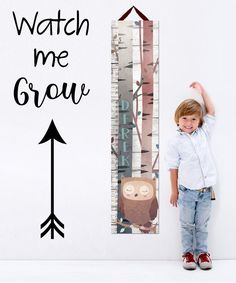 a little boy standing next to a growth chart with an owl on it's back