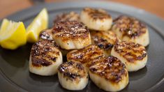 some scallops are sitting on a plate with lemon wedges