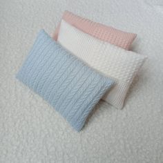 three knitted pillows laying on top of a white bed sheet with blue and pink accents