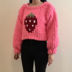 a woman standing in front of a wall wearing a pink sweater with strawberries on it