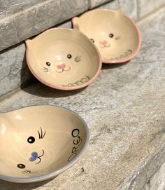 two ceramic bowls with cats painted on them sitting next to each other in front of a stone wall