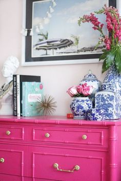 a pink dresser with blue and white vases on it's top next to a painting