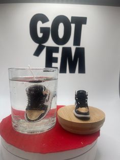 a pair of shoes sitting on top of a wooden stand next to a glass cup