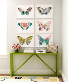 a green table topped with lots of butterflies on top of a white wall next to a window